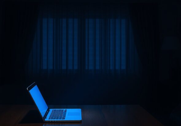 A quiet, dimly lit living room at night with a single laptop open on a wooden table, casting a soft blue glow on an empty chair, moody atmosphere, cinematic lighting, high resolution, photorealistic style.
